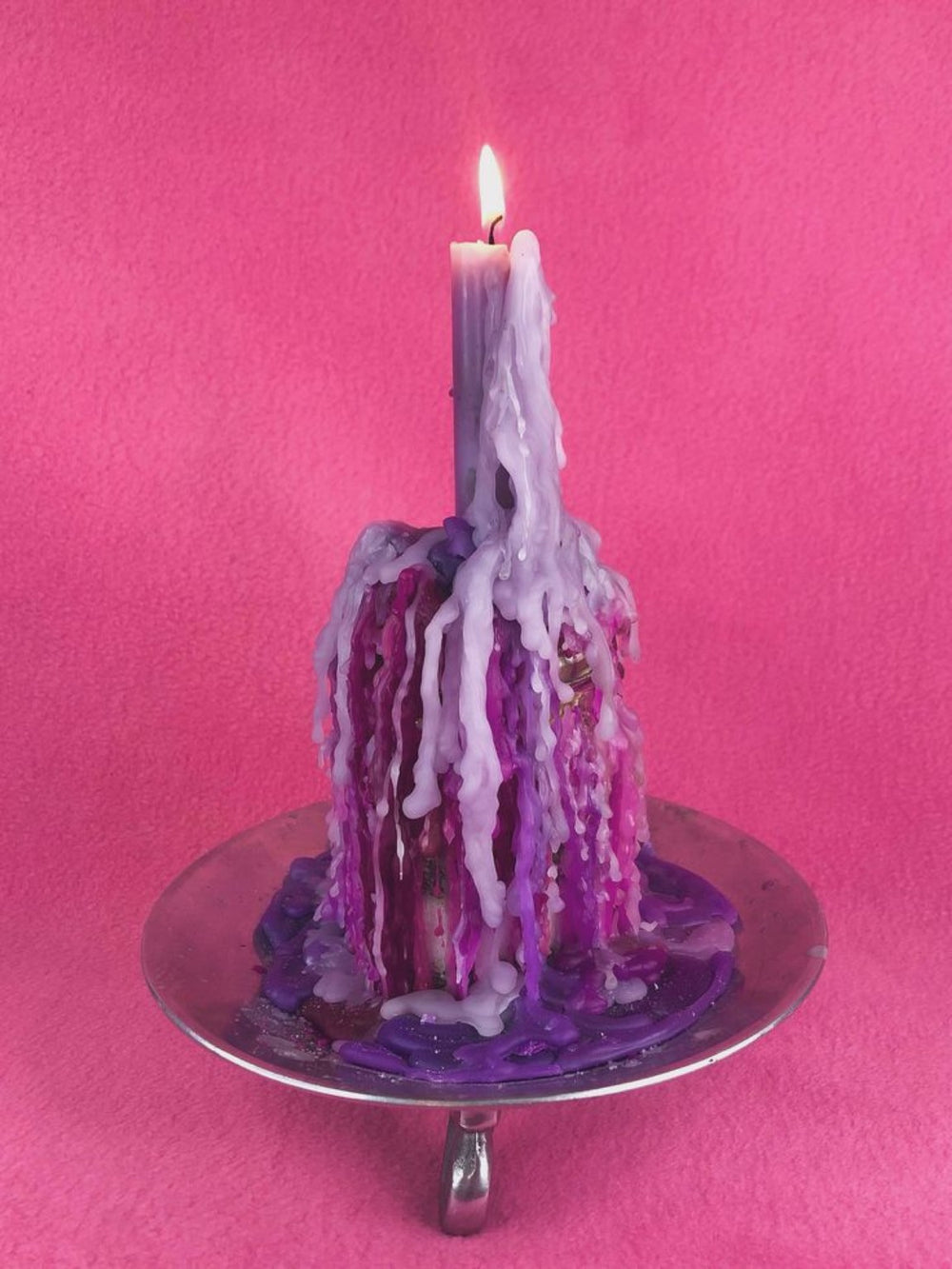 Lit lavender candle with layers of purple wax draped over a glass bottle against pink fabric